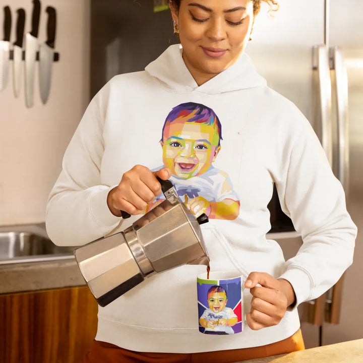 Person pouring coffee from a French press into a mug with a colorful baby design, wearing a white hoodie with a similar design.